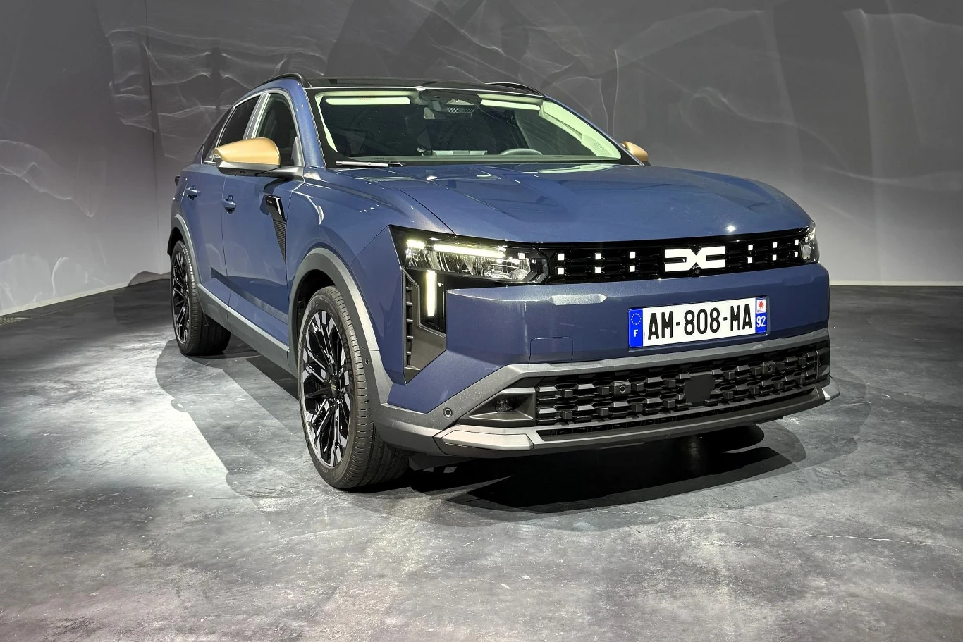 Niebieski miejski SUV o dynamicznej sylwetce, nowoczesnych reflektorach LED i czarnych, sportowych felgach, z białą tablicą rejestracyjną umieszczoną z przodu pojazdu.