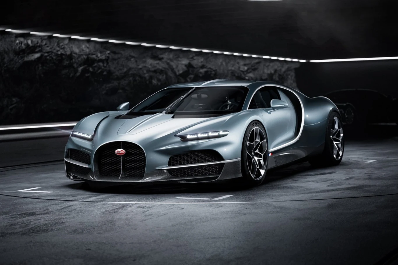 Luksusowy, srebrny sportowy samochód Bugatti Chiron z charakterystycznym logo na grillu, dynamicznymi liniami nadwozia i nowoczesnym oświetleniem LED, ustawiony na betonowej powierzchni w ciemnym, industrialnym otoczeniu.