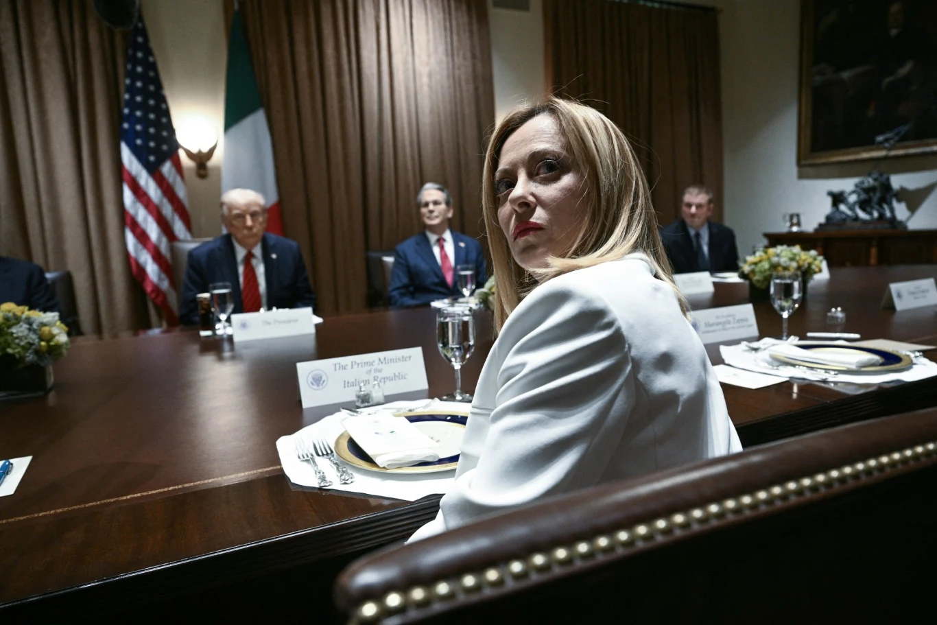 Giorgia Meloni kontra Donald Trump. Premier nie reaguje na prowokację prezydenta USA Giorgia Meloni przy stole konferencyjnym, obok politycy, w tle flagi USA i Włoch