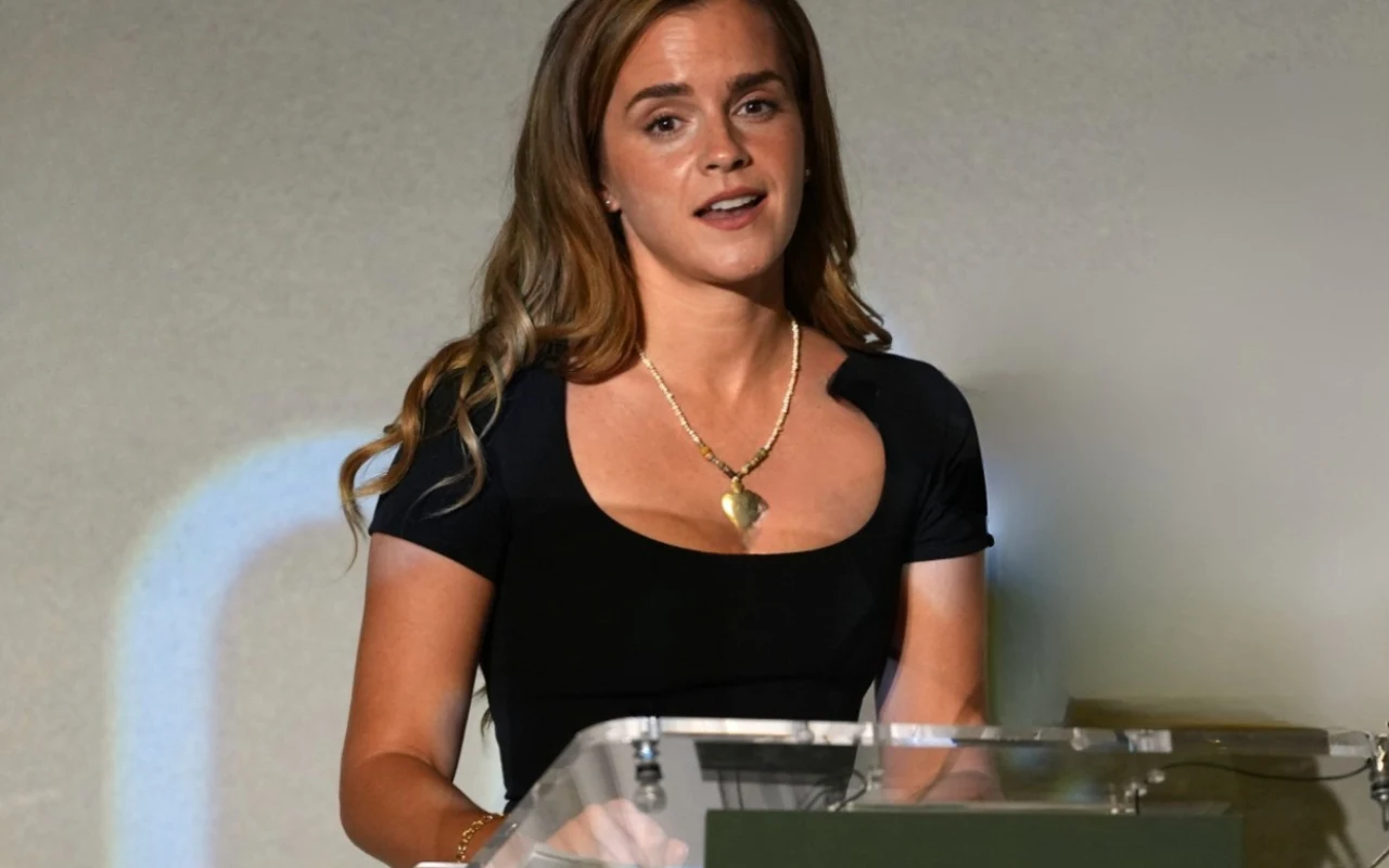 Emma Watson na forum biznesowym, czerwiec 2026 Kobieta z długimi, falującymi włosami w czarnej sukience stoi za przezroczystą mównicą i mówi, trzymając jedną rękę na pulpicie.