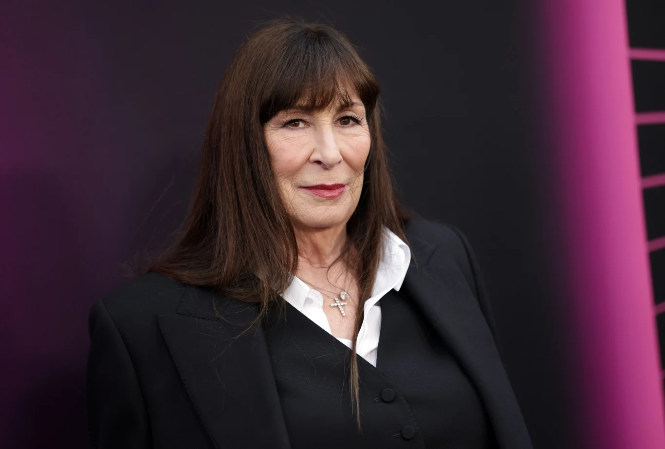 Anjelica Huston obchodzi 75. urodziny Anjelica Huston w czarnym garniturze i białej koszuli na tle ciemnej ściany z fioletowym akcentem.