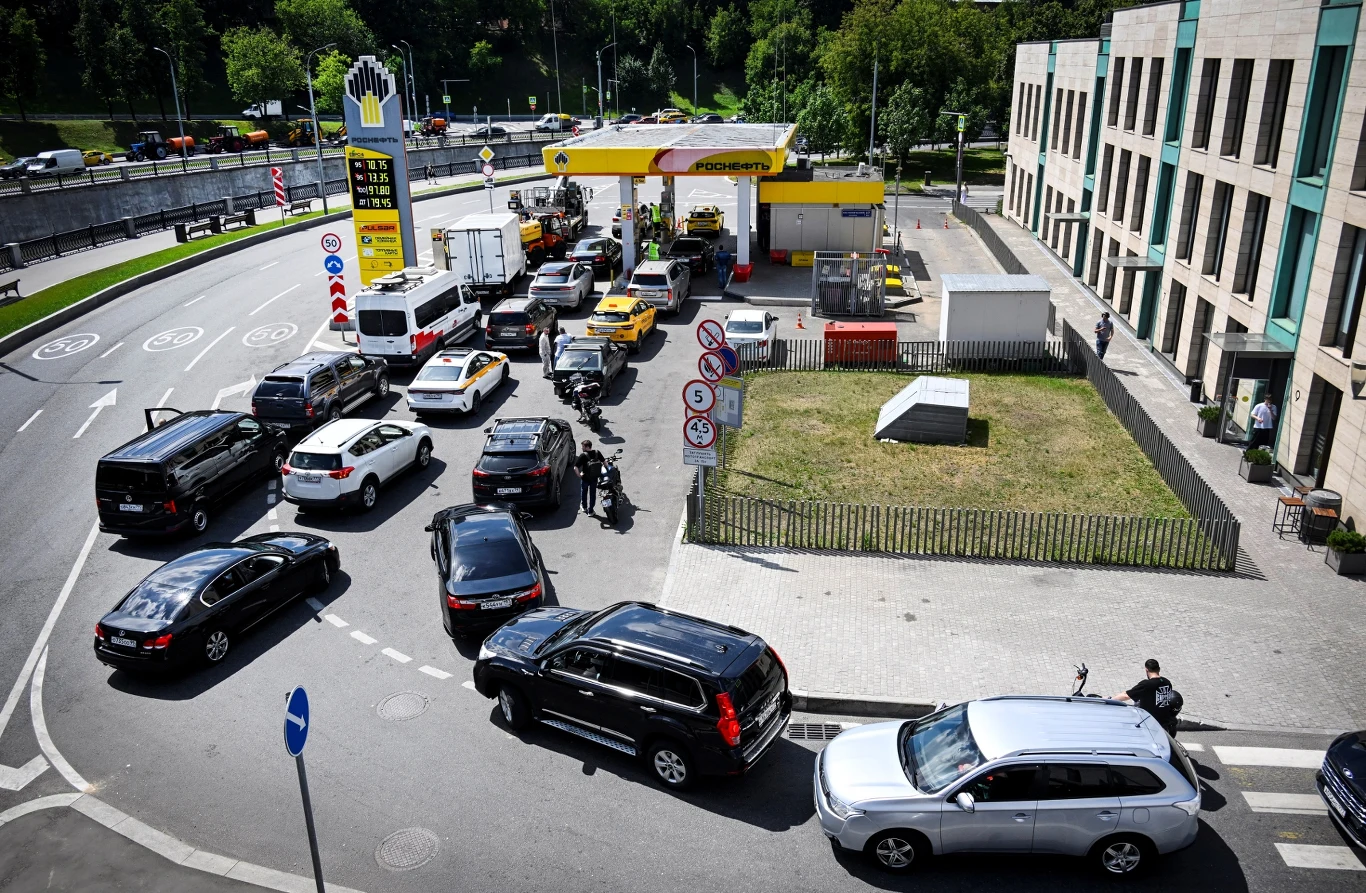 Braki paliwa nie omijają nawet regionu moskiewskiego Długa kolejka samochodów ustawionych przed stacją benzynową, większość pojazdów czeka na możliwość zatankowania, a na terenie stacji widoczne są dystrybutory paliw oraz kilku przechodniów i pracowników.