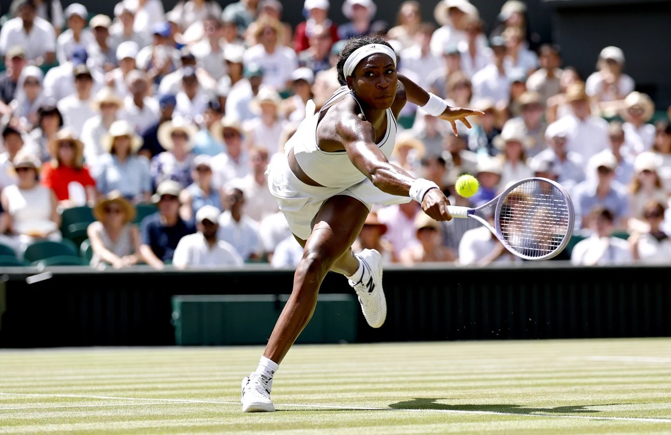 Coco Gauff Tenisistka w stroju sportowym dynamicznie sięga rakietą po piłkę na trawiastym korcie podczas meczu, wokół zgromadzona widownia.