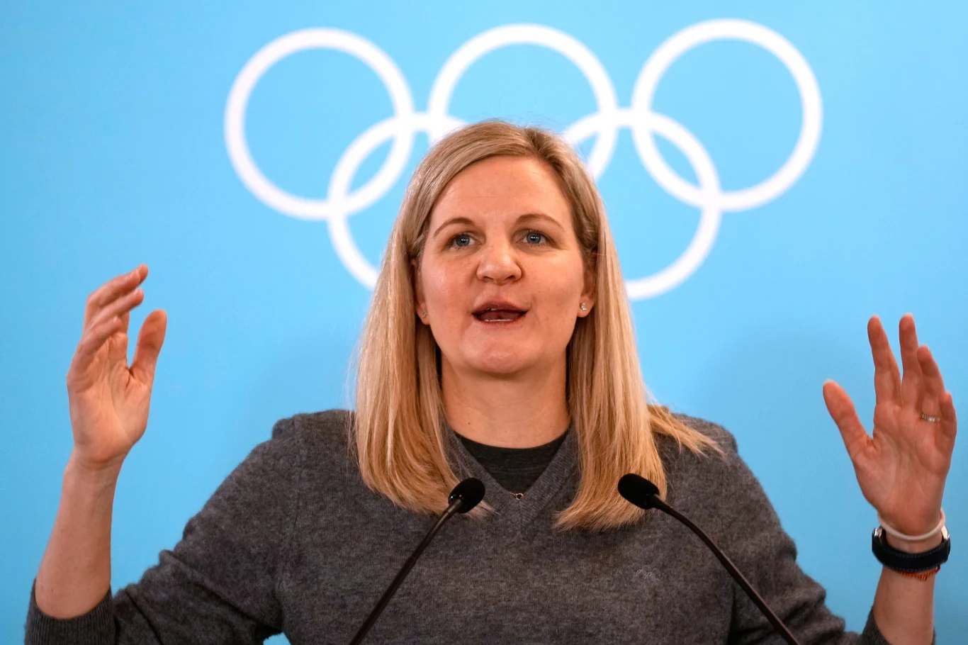 Rosjanie mogą wrócić do rywalizacji międzynarodowej Kobieta o blond włosach przemawia przy dwóch mikrofonach na tle niebieskiej ściany z widocznym symbolem olimpijskich kół.