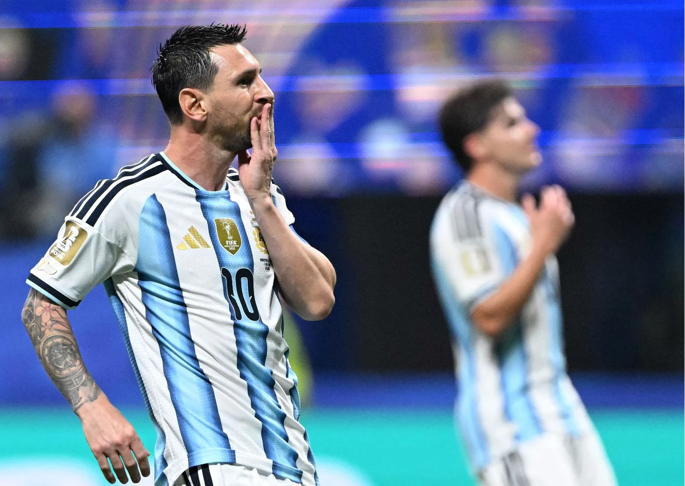 Piłkarz reprezentacji Argentyny w jasnoniebiesko-białej koszulce z numerem dziesięć wykonuje gest ręką przy ustach, a drugi zawodnik w tle także okazuje emocje na boisku.