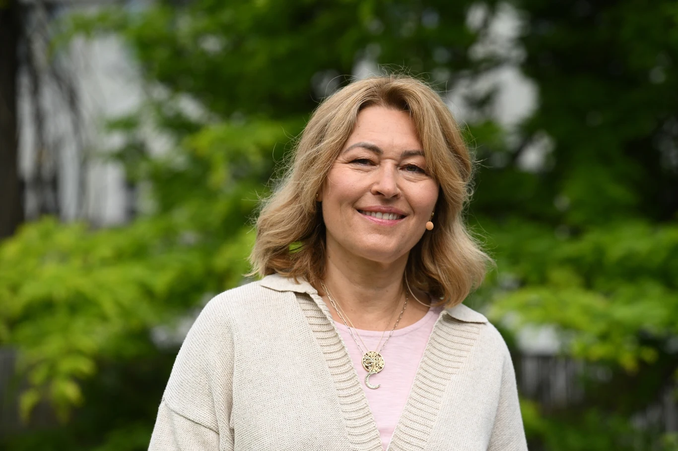 Beata Sadowska wróciła jako gość "Pytania na śniadanie" Uśmiechnięta kobieta z jasnymi włosami, ubrana w jasny sweter, stoi na tle zielonych liści drzew.