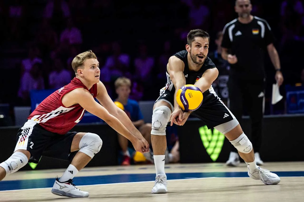 Dwóch siatkarzy w sportowych strojach dynamicznie odbija piłkę podczas meczu, skupieni na precyzji zagrania.