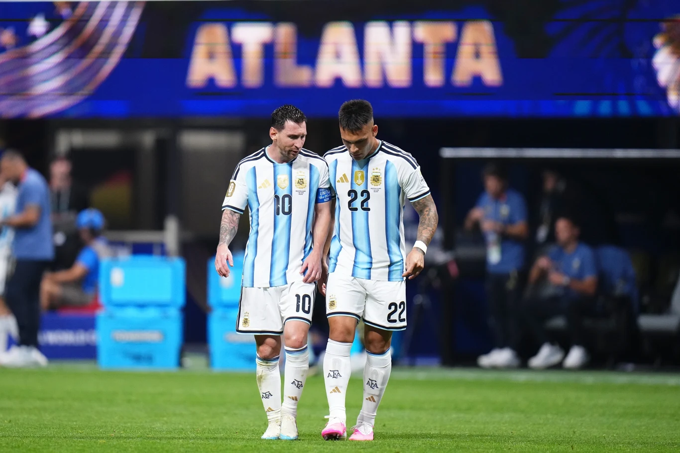 Dwóch piłkarzy w biało-niebieskich strojach Argentyny idzie ramię w ramię po murawie stadionu, na tle dużego napisu ATLANTA.