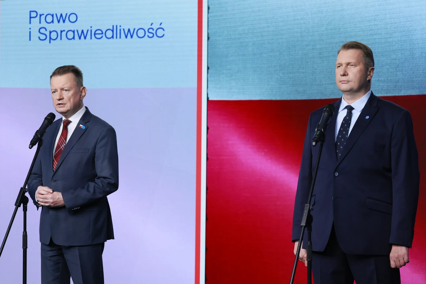 Mariusz Błaszczak i Przemysław Czarnek podczas konferencji prasowej Mariusz Błaszczak i Przemysław Czarnek podczas konferencji prasowej przy mikrofonach na tle flagi Polski i logo PiS