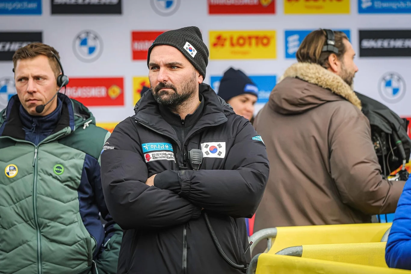 Maciej Kurowski Maciej Kurowski w kurtce Korei Południowej stoi z mężczyzną w zielonej kurtce na tle bannerów sponsorów