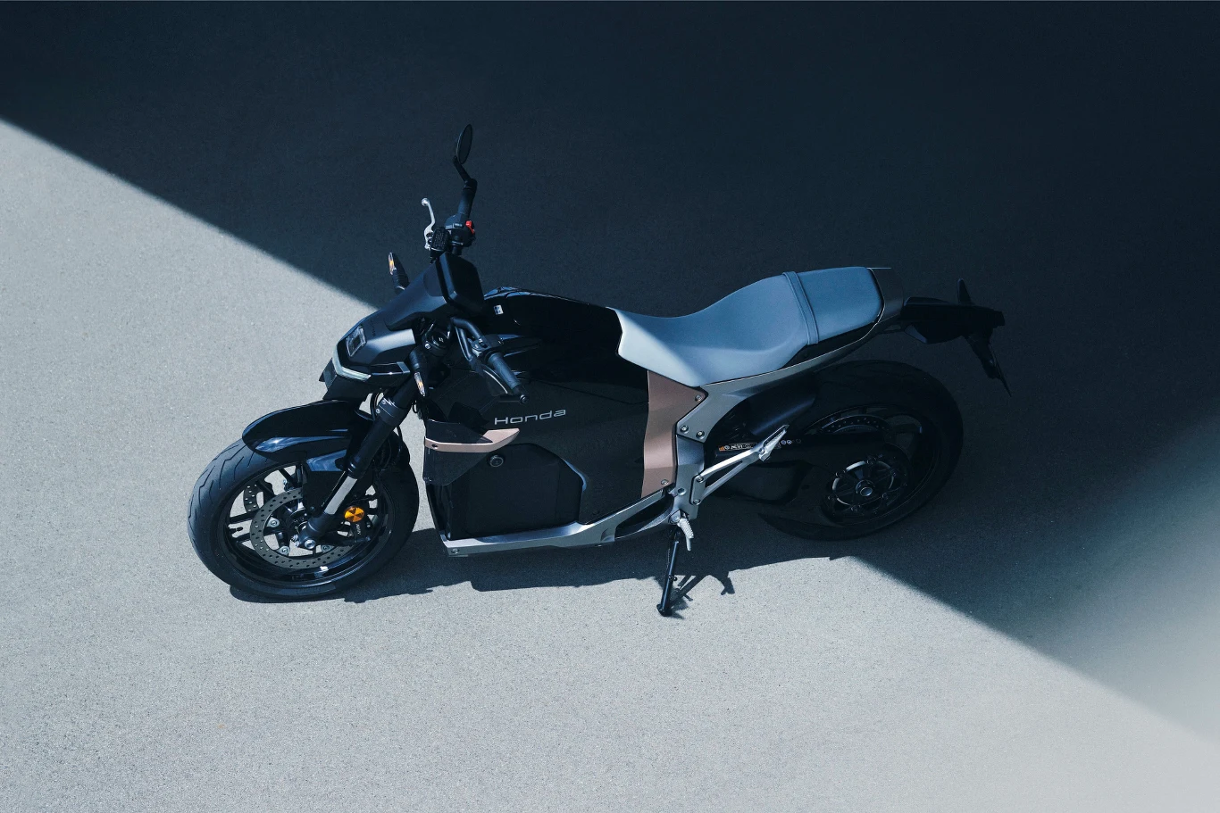 Czarny motocykl elektryczny marki Horwin ustawiony na jasnym, betonowym podłożu, oświetlony kontrastowym promieniem światła.