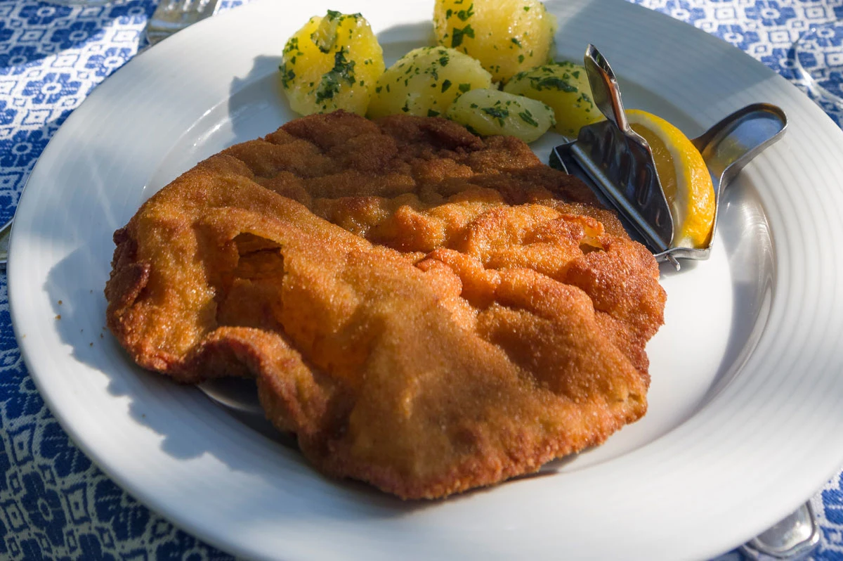 Wiener Schnitzel to w Austrii nazwa prawnie chroniona. Danie może być zrobione tylko z cielęciny Sznycel panierowany z ziemniakami na białym talerzu. do tego ćwiartka cytryny do wyciśnięcia