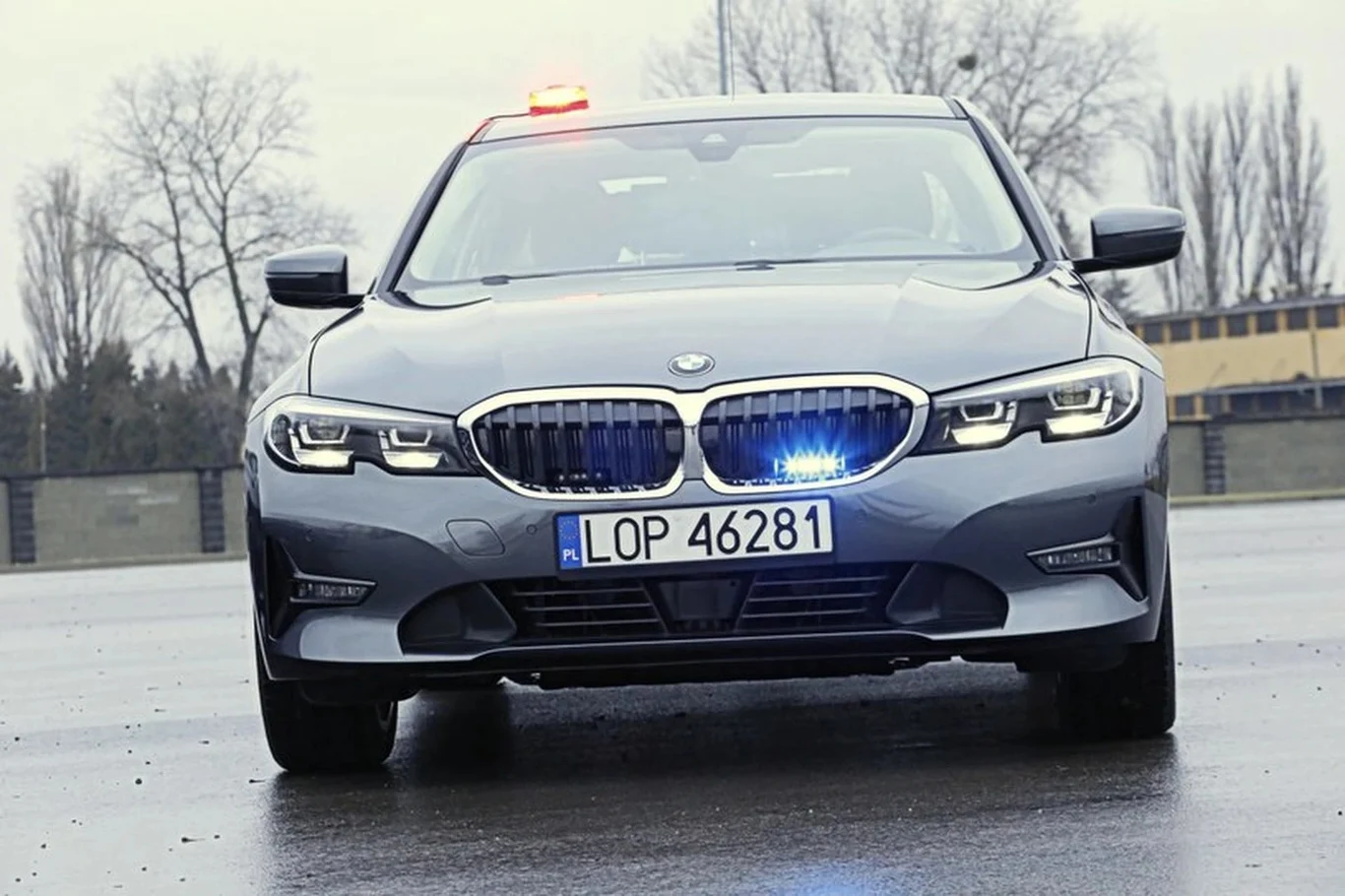 Po czym rozpoznać nieoznakowany radiowóz policyjny grupy Speed? Policyjny nieoznakowany radiowóz BMW z włączonymi sygnałami świetlnymi, przód pojazdu na mokrej drodze.