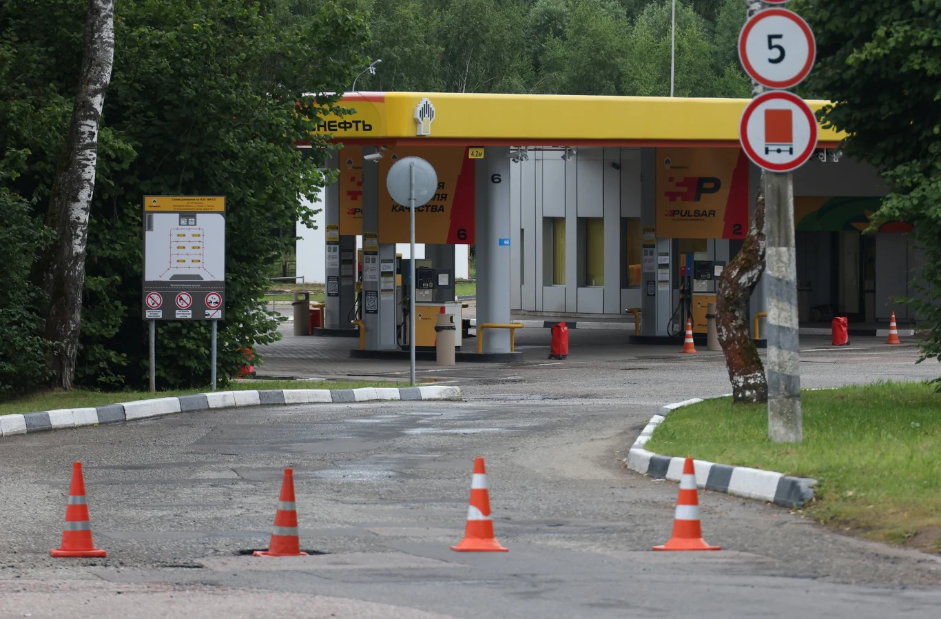 Taki widok w Rosji to coraz częstszy widok Stacja benzynowa otoczona zielenią, z pachołkami drogowymi blokującymi wjazd oraz znakami ograniczenia prędkości i zakazu wjazdu dla pojazdów ciężarowych.