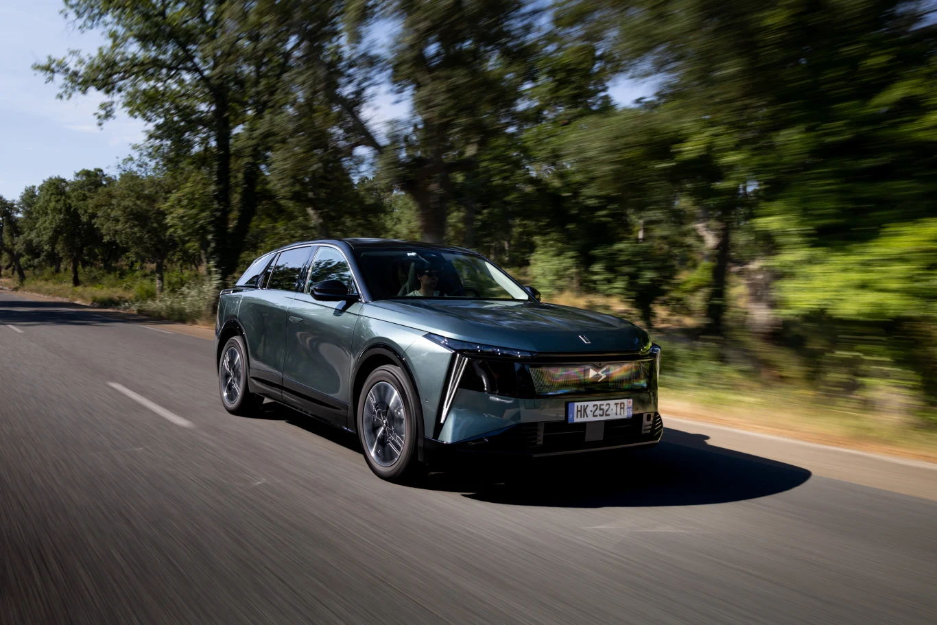 Nowoczesny, zielony SUV jadący drogą otoczoną drzewami, dynamiczny ujęcie podkreślające ruch pojazdu.