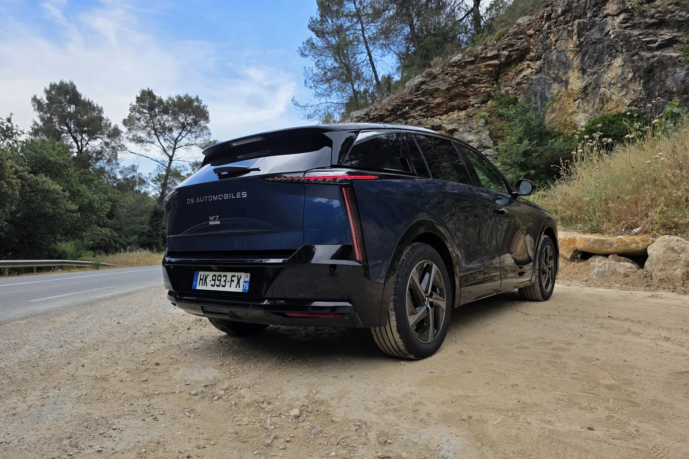 Czarny SUV DS Automobiles zaparkowany na żwirowej drodze przy skalistym wzniesieniu, w otoczeniu drzew i roślinności śródziemnomorskiej.