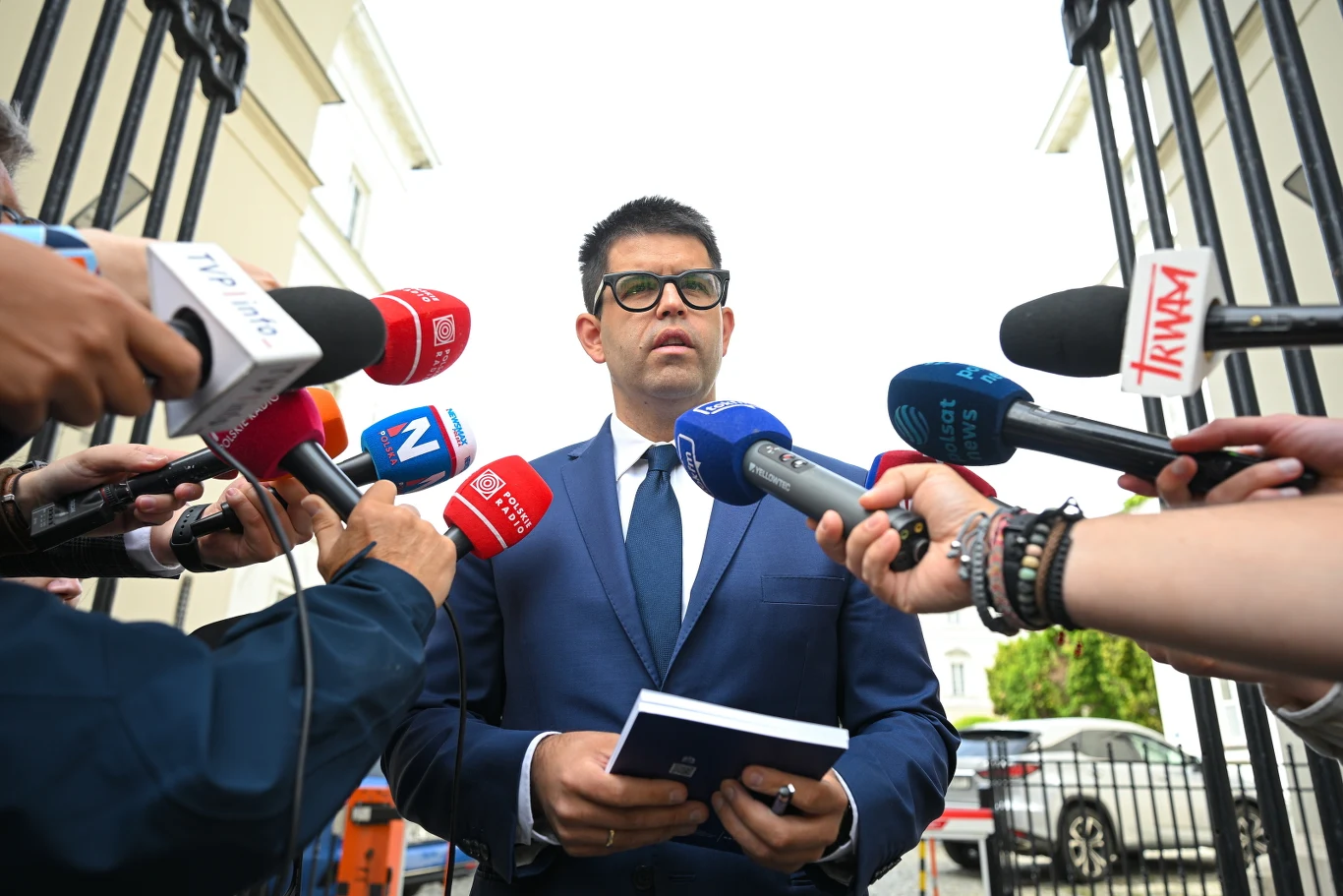 Łukasz Jankowski, prezes Naczelnej Izby Lekarskiej Łukasz Jankowski, prezes NIL, w garniturze i okularach, udziela wypowiedzi mediom przed mikrofonami.