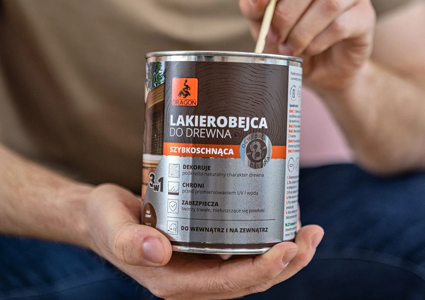 Lakierobejca Dragon Puszka lakierobejcy do drewna marki Dragon trzymana w ręce, z widoczną etykietą informującą o szybkoschnącym produkcie zabezpieczającym drewno.