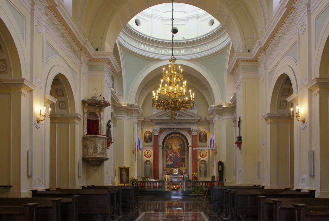 14 lipca Kościół obchodzi podwójne wspomnienie świętych Wnętrze kościoła katolickiego z wysokimi łukami, złoconym żyrandolem i zdobionym ołtarzem ze świętymi obrazami