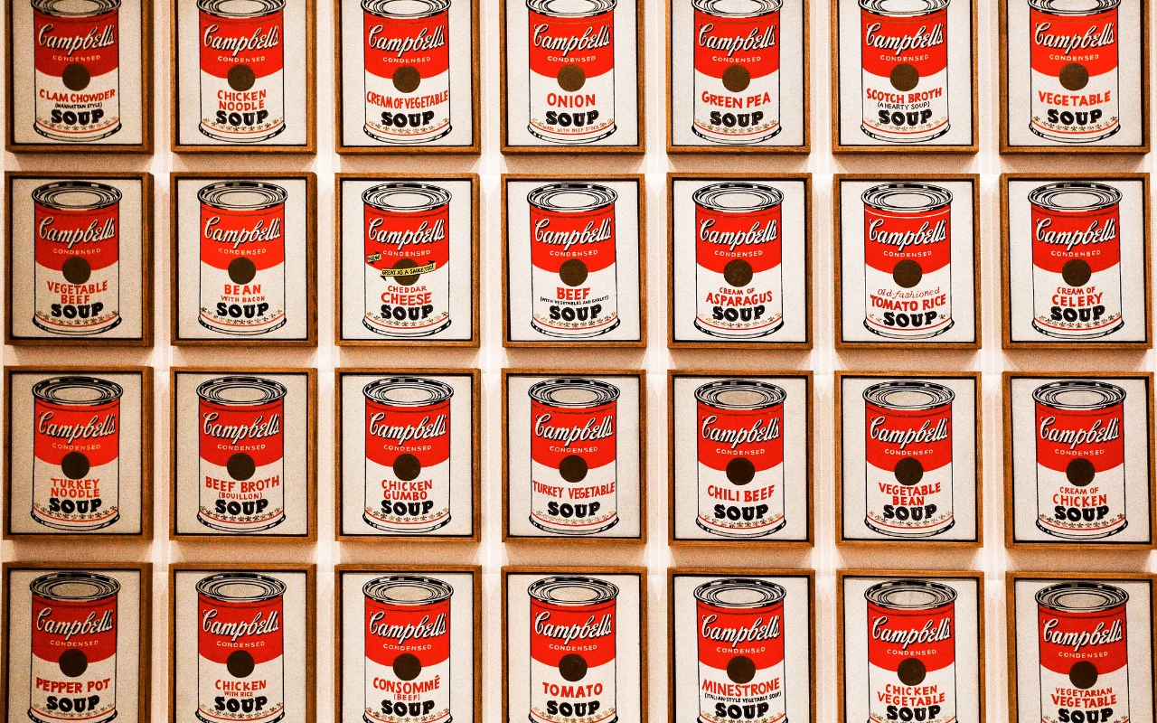 "Campbell’s Soup Cans" Andy'ego Warhola Obrazy Andy'ego Warhola z motywem puszek zupy Campbell’s, w regularnej siatce, z widocznymi nazwami różnych smaków zup.