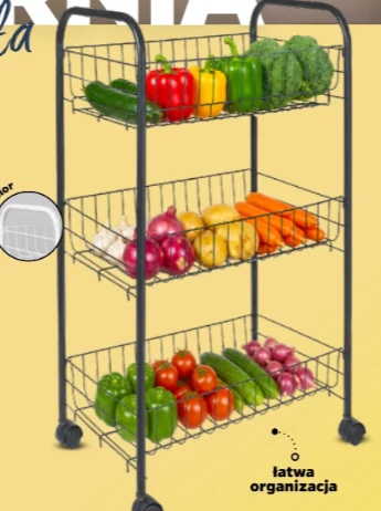 Trójpoziomowy metalowy regał na kółkach z koszami wypełnionymi różnymi warzywami, takimi jak papryka, ogórki, brokuły, cebula, ziemniaki, marchew oraz pomidory.