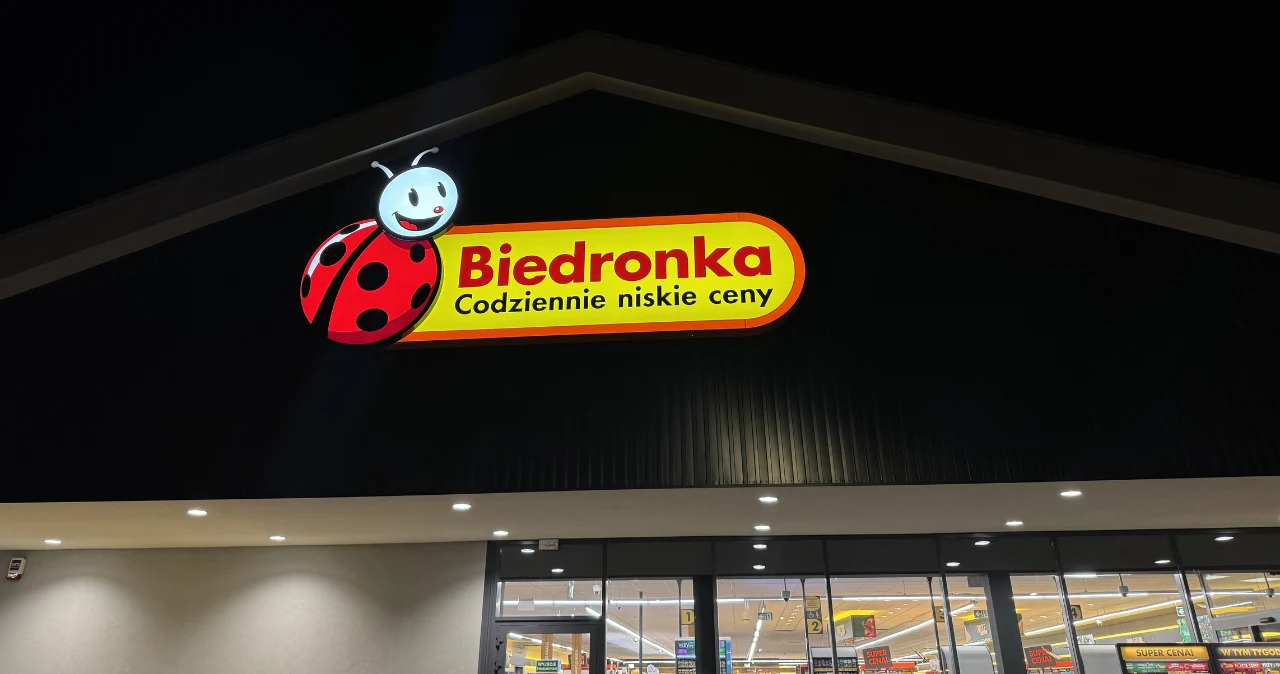 Walizki, plecaki i organizery. Biedronka przygotowała ofertę dla osób planujących wakacje Sklep Biedronka nocą z podświetlanym logo sieci na elewacji budynku.