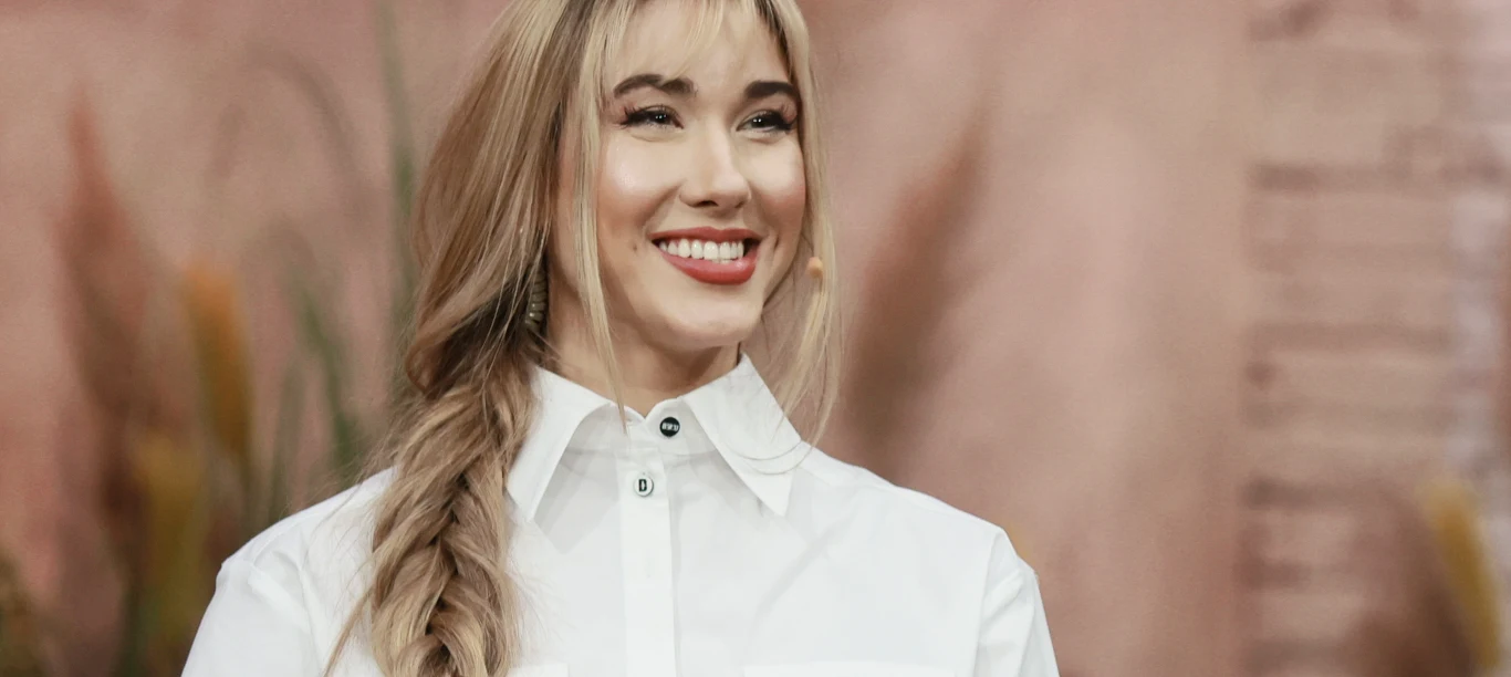 Ida Nowakowska Ida Nowakowska w białej koszuli, z długimi blond włosami w warkoczu, na tle jasnego wnętrza.