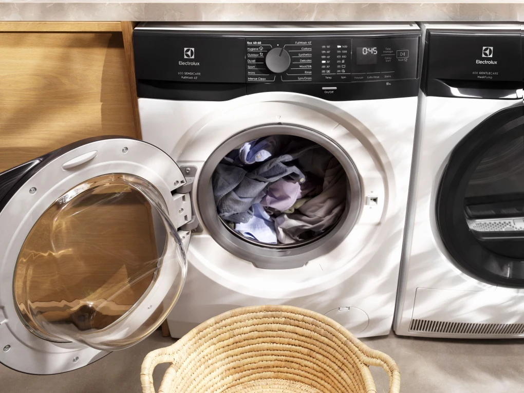 Najszybsze pranie przy pełnym załadunku. Czyste ubrania w 45 minut w temperaturze 30°C z programem FullWash Pralka o otwartych drzwiach z widoczną partią kolorowego prania w bębnie, obok której stoi kosz na ubrania.