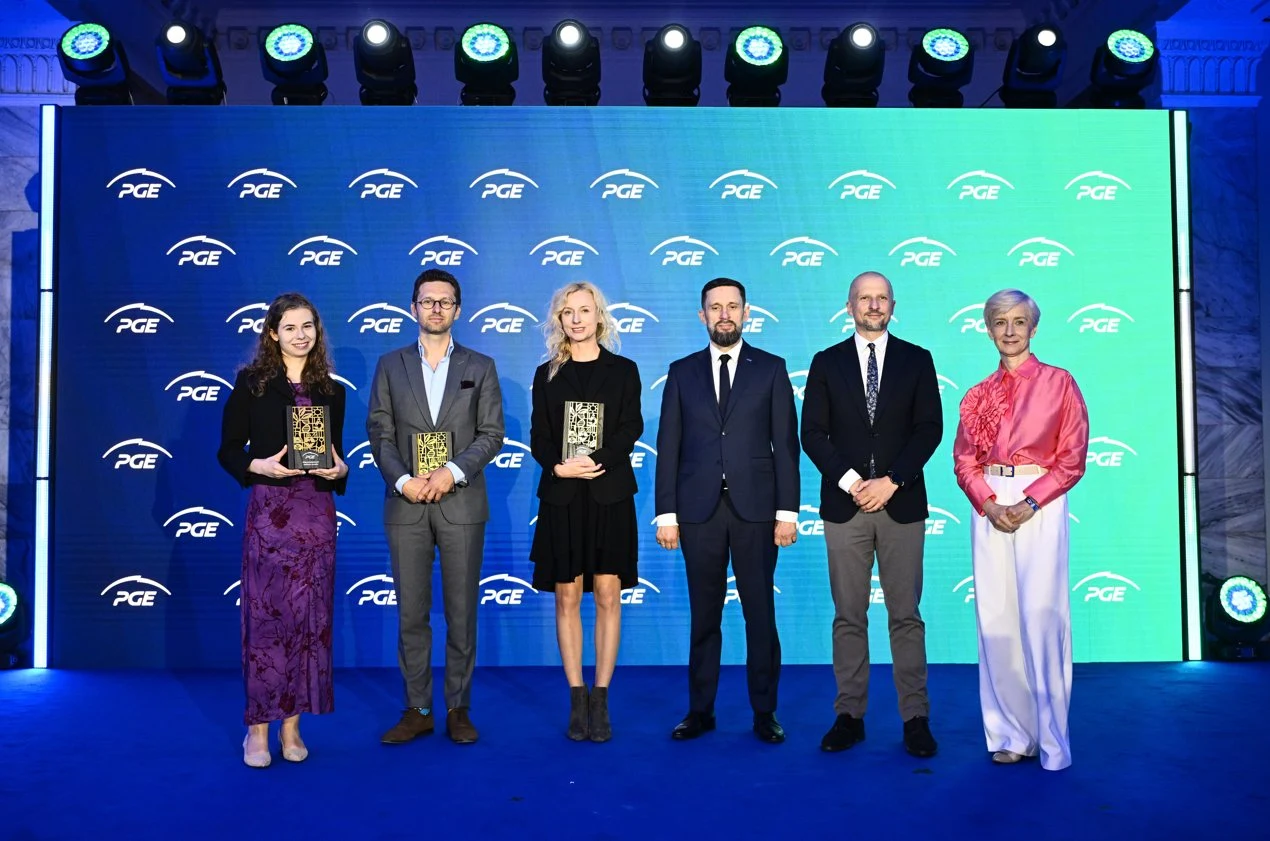 Sześć osób ustawionych w szeregu na niebieskim tle z logo PGE, trzy z nich trzymają w dłoniach statuetki.