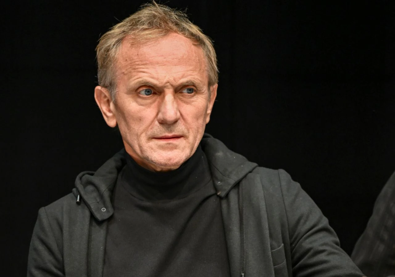 Andrzej Chyra Mężczyzna o poważnym wyrazie twarzy w czarnym golfie i kurtce, na ciemnym tle.