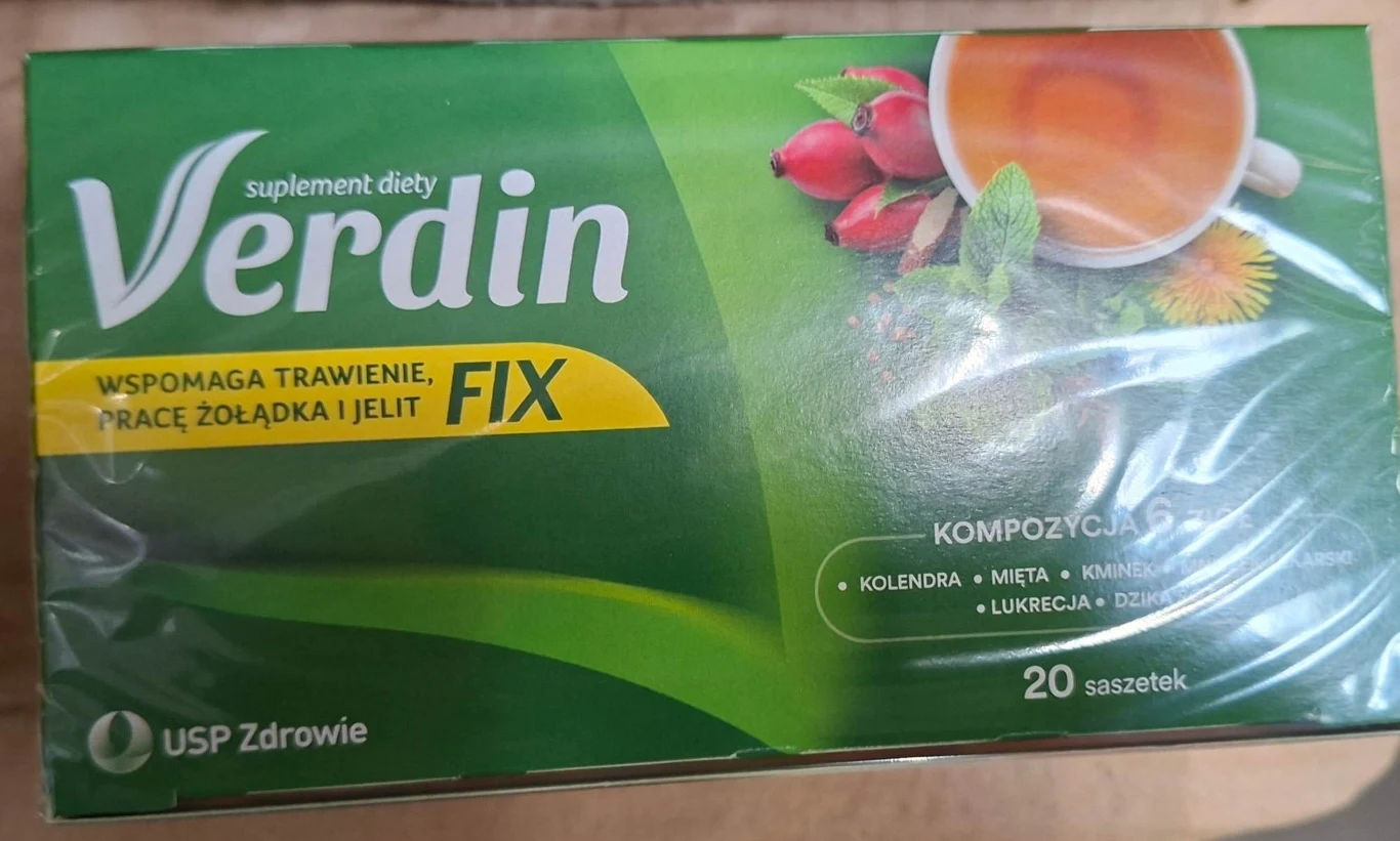 Zielone opakowanie herbaty Verdin Fix, z widocznym napisem o wspomaganiu trawienia oraz grafiką filiżanki ziołowego naparu i gałązki kolendry obok owoców dzikiej róży, informacja o 20 saszetkach i producencie USP Zdrowie.