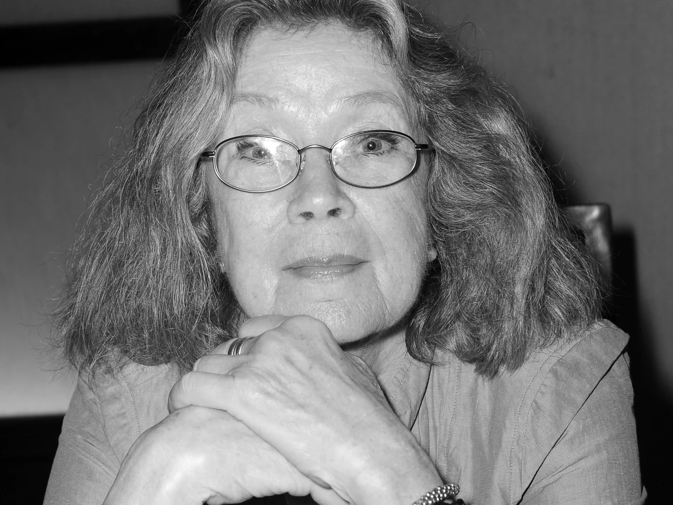 Antoinette Bower nie żyje Starsza kobieta z okularami, o jasnych, półdługich włosach, opiera brodę na splecionych dłoniach i patrzy prosto w obiektyw.