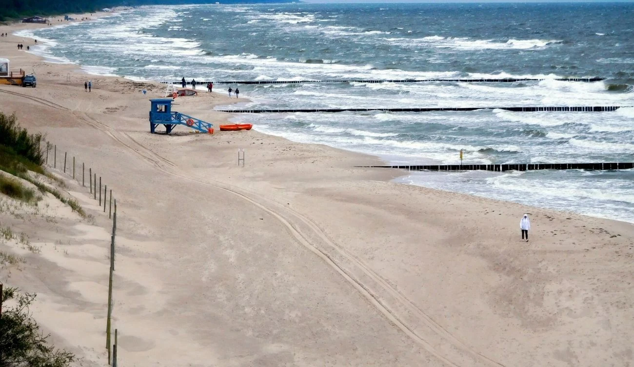 "Płonący bursztyn" jest łatwy do pomylenia z prawdziwym bursztynem Szeroka plaża ze spacerowiczami, wzburzone morze, niebieska budka i drewniane falochrony.