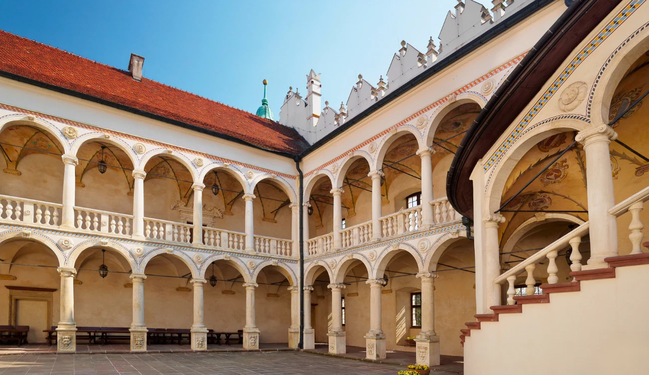 Jaka jest historia zamku w Baranowie Sandomierskim? Zabytkowy dziedziniec z dwupoziomowymi arkadami, renesansowymi kolumnami oraz dekoracyjnymi balustradami, otoczony czerwonym dachem i bogato zdobionymi fasadami.
