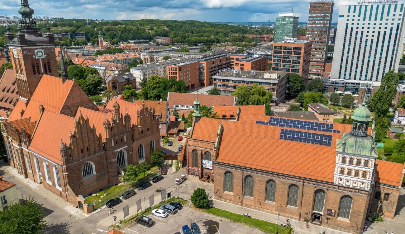 Zjawisko miejskich wysp ciepła nasila się z każdym rokiem Widok na Gdańsk w słoneczną pogodę z widocznymi panelami fotowoltaicznymi na dachu Bazyliki sw. Brgydy.