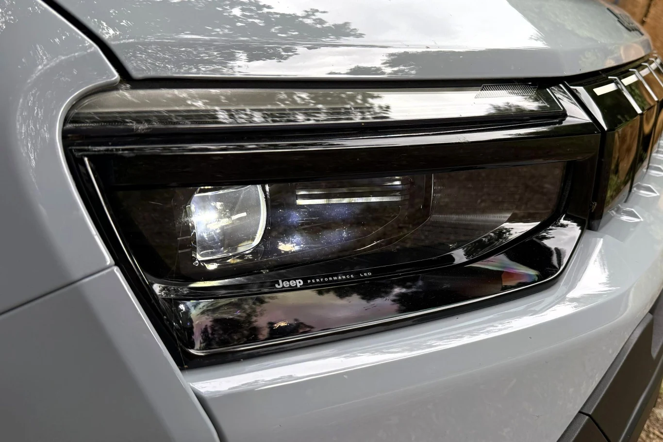 Zbliżenie na reflektor LED nowoczesnego samochodu marki Jeep w srebrnym kolorze, z widocznymi detalami obudowy lampy i odbiciem otoczenia.