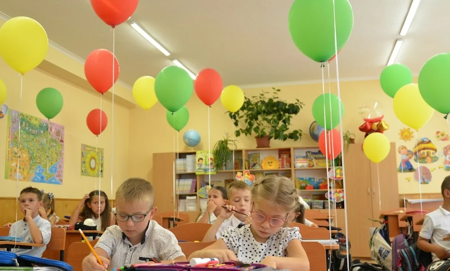 Wyprawka szkolna 2026 — dzieci w klasie na starcie roku szkolnego Dzieci piszące w zeszytach w kolorowej klasie z balonami — początek roku szkolnego 2026