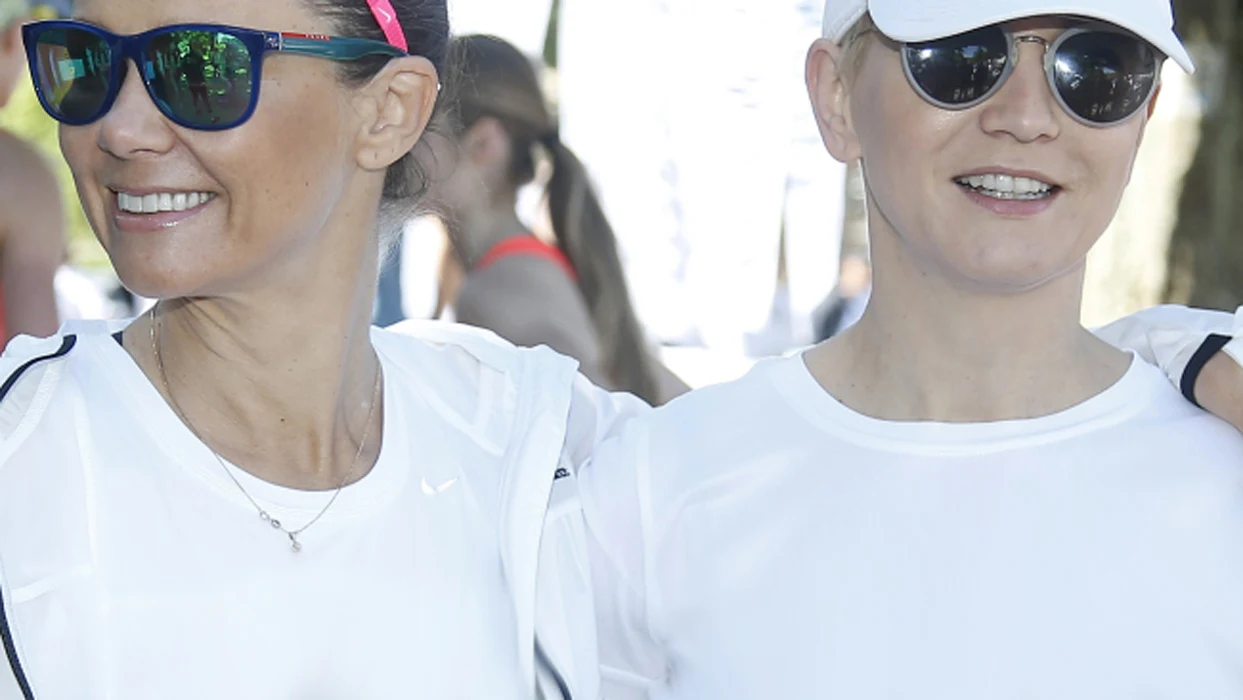 Dwie uśmiechnięte kobiety w sportowych okularach przeciwsłonecznych i jasnych koszulkach pozują razem na świeżym powietrzu.