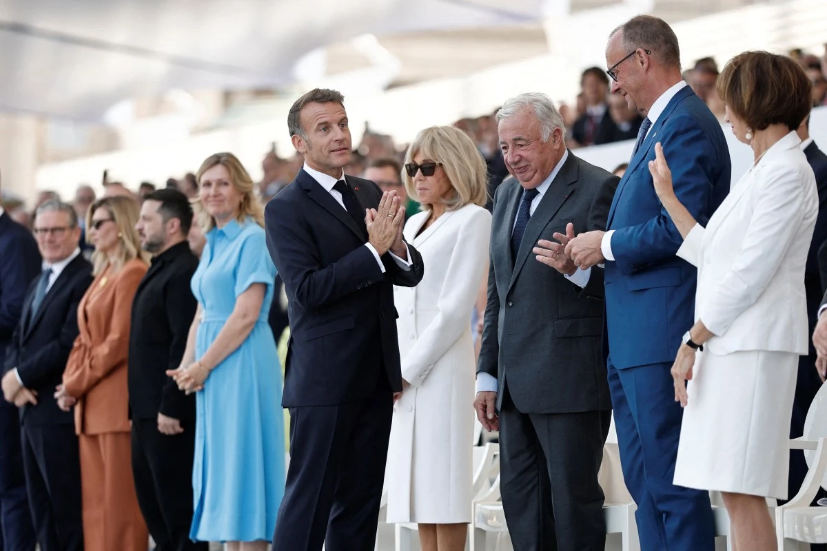 Grupa elegancko ubranych osób stojących w rzędzie, skupionych wokół mężczyzny w garniturze gestykulującego w rozmowie z innymi uczestnikami uroczystości.