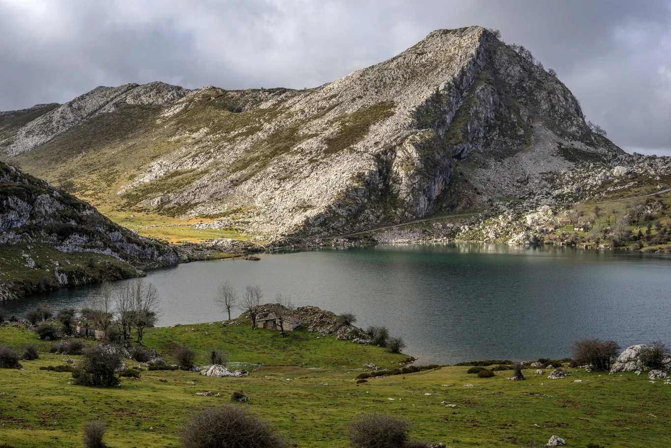 Park Narodowy Picos de Europa to nie tylko góry, ale też jeziora polodowcowe, spektakularne wąwozy oraz urokliwe górskie wioski. Jezioro otoczone stromymi, skalistymi górami, w dolinie pokrytej zieloną trawą z pojedynczymi drzewami i krzewami.