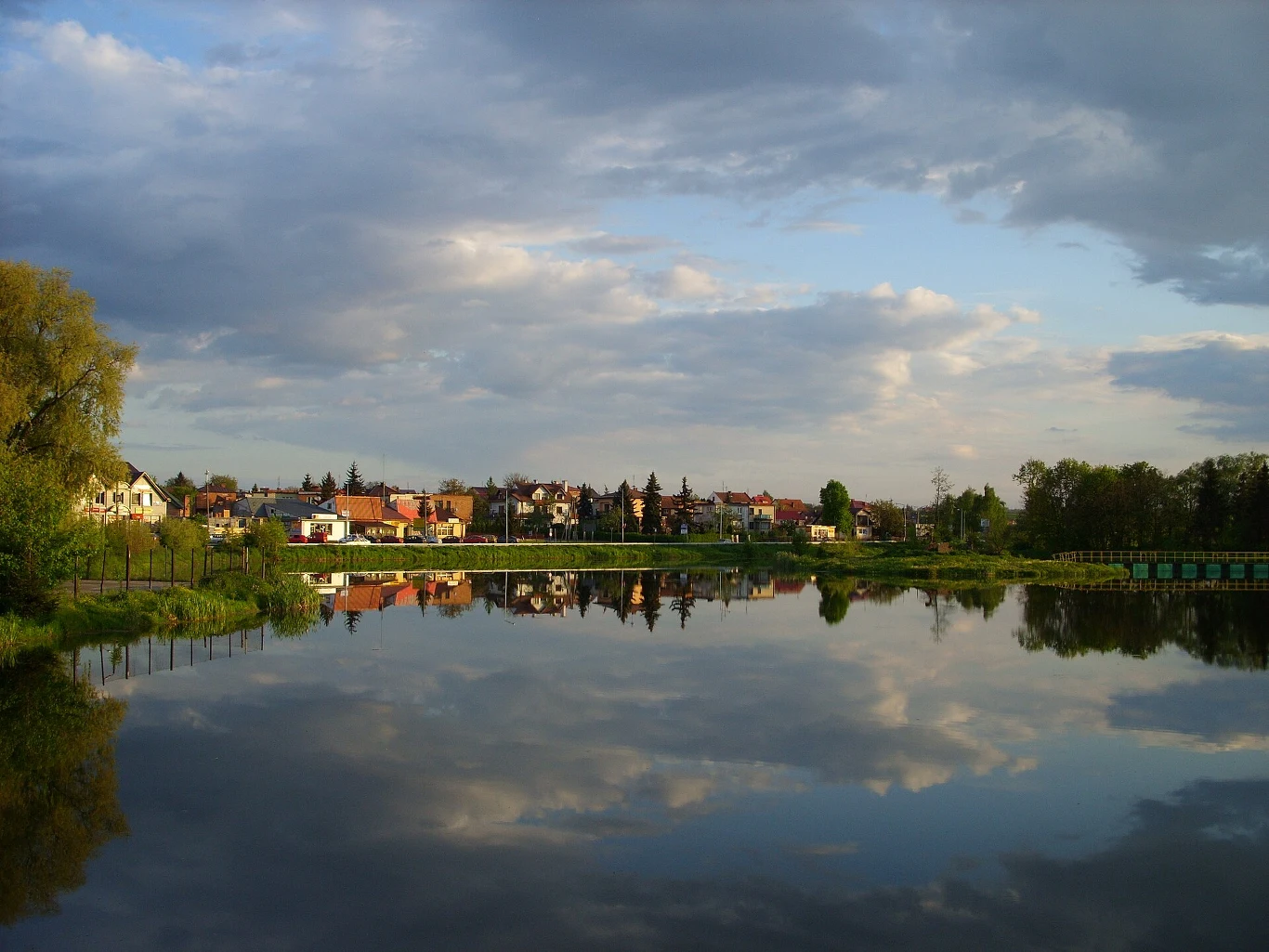 zdj. Luk123KW, CC-By-SA 4.0, via Wikimedia Commons; Kazimierza Wielka może stać się uzdrowiskiem Kazimierza Wielka, jezioro z odbiciem chmur, w tle domy i niska zabudowa w otoczeniu zieleni