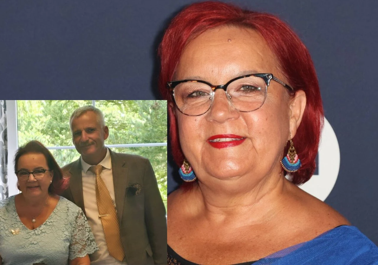 Kobieta w czerwonych włosach i okularach z delikatnym uśmiechem pozuje na tle ciemnoniebieskiej ściany, a w lewym dolnym rogu widoczna jest ta sama kobieta oraz mężczyzna w eleganckich ubraniach, stojący razem przy oknie.