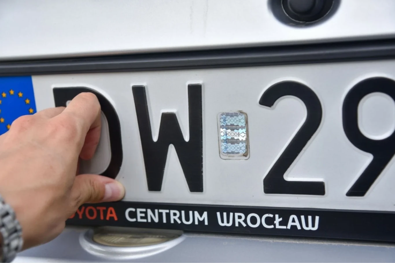 Tablica rejestracyjna z kodem województwa dolnośląskiego, trzymana przez lewą dłoń osoby, pod ramką z napisem 'Toyota Centrum Wrocław'.