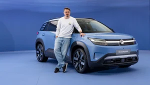 Mężczyzna w swobodnym stroju opiera się o błękitnego SUV-a marki Volkswagen ID. Cross, prezentowanego w minimalistycznej scenerii o niebieskiej kolorystyce.