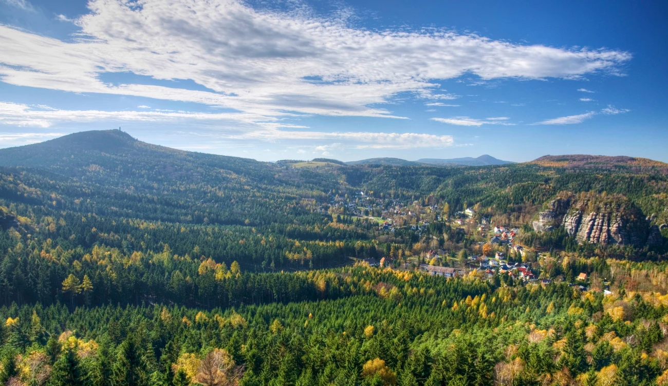 Gdzie są Góry Łużyckie? Panorama Gór Łużyckich z lasami, osadą w dolinie i skalistymi wzgórzami na tle nieba z chmurami.