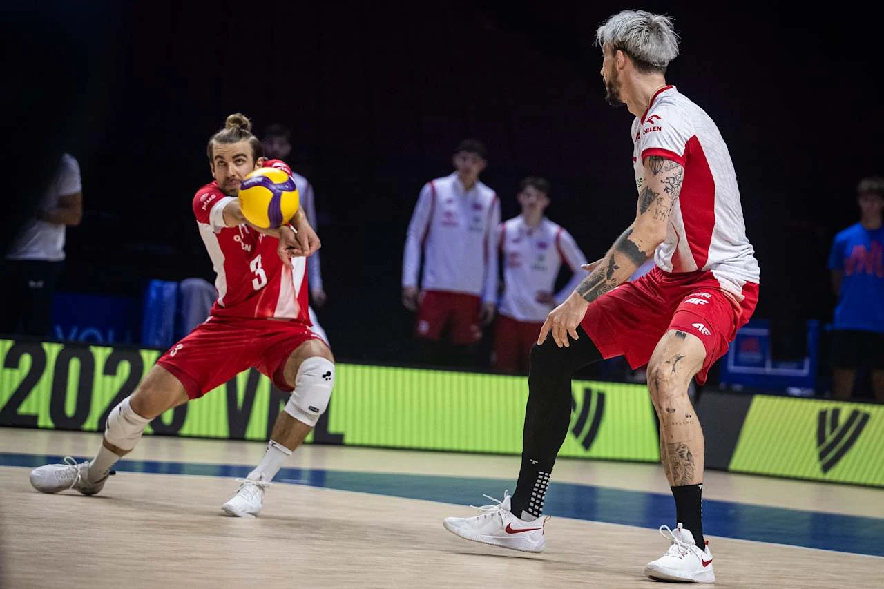 Jakub Popiwczak w meczu z Bułgarią Dwóch siatkarzy w biało-czerwonych strojach podczas intensywnej akcji; jeden z zawodników wybija piłkę w przyjęciu, drugi jest gotowy do reakcji, w tle widoczna reszta drużyny.