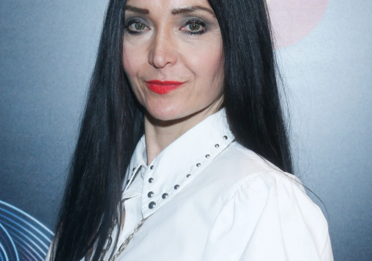 Alicja Walczak z "Big Brothera" Alicja Walczak, uczestniczka pierwszej edycji programu Big Brother, w białej koszuli na tle geometrycznej grafiki.
