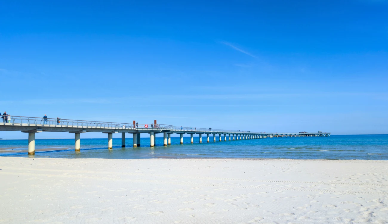 Jakie jest najdłuższe molo nad Bałtykiem? Długie molo nad Morzem Bałtyckim, rozciągające się nad wodą obok piaszczystej plaży pod jasnym niebem.