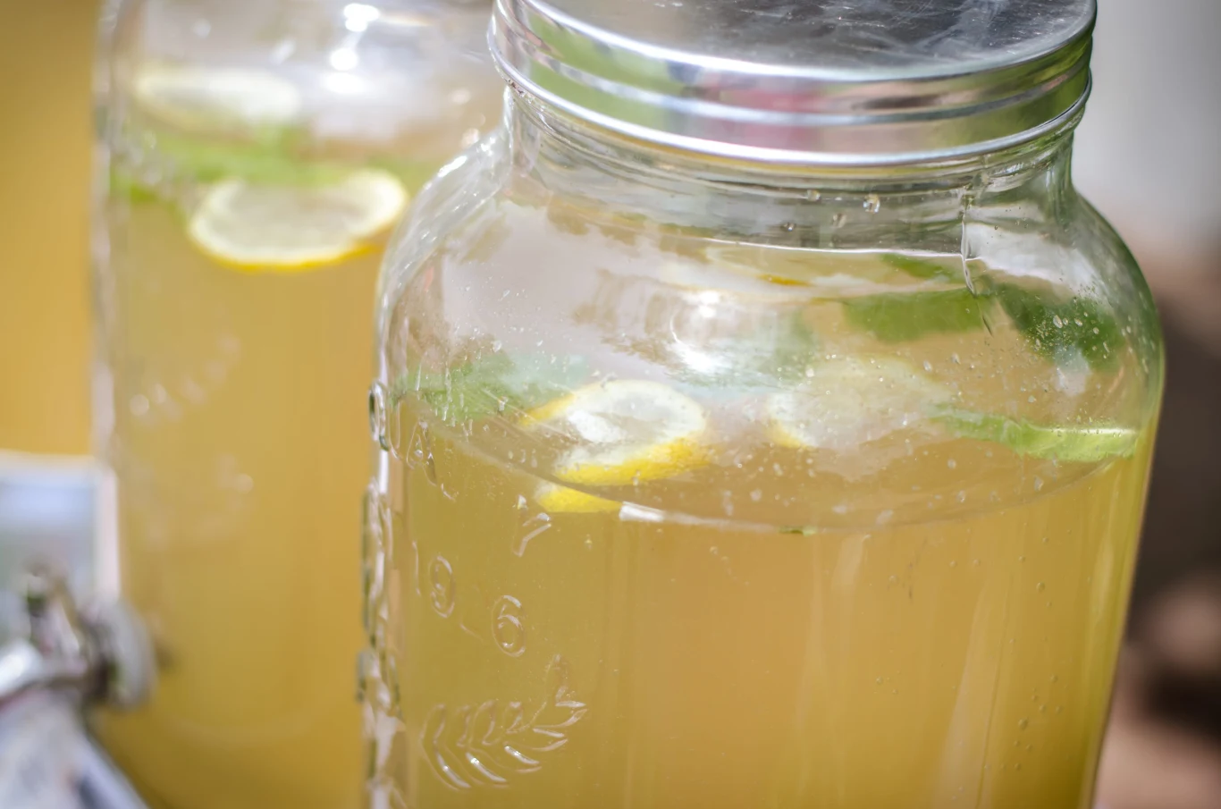 Lemoniada z drożdżami w zamkniętym naczyniu dzięki fermentacji zyskuje efekt musowania. /Fot. katarinagondova/123RF Słoik z metalową pokrywką, wypełniony lemoniadą z plasterkami cytryny i liśćmi mięty.