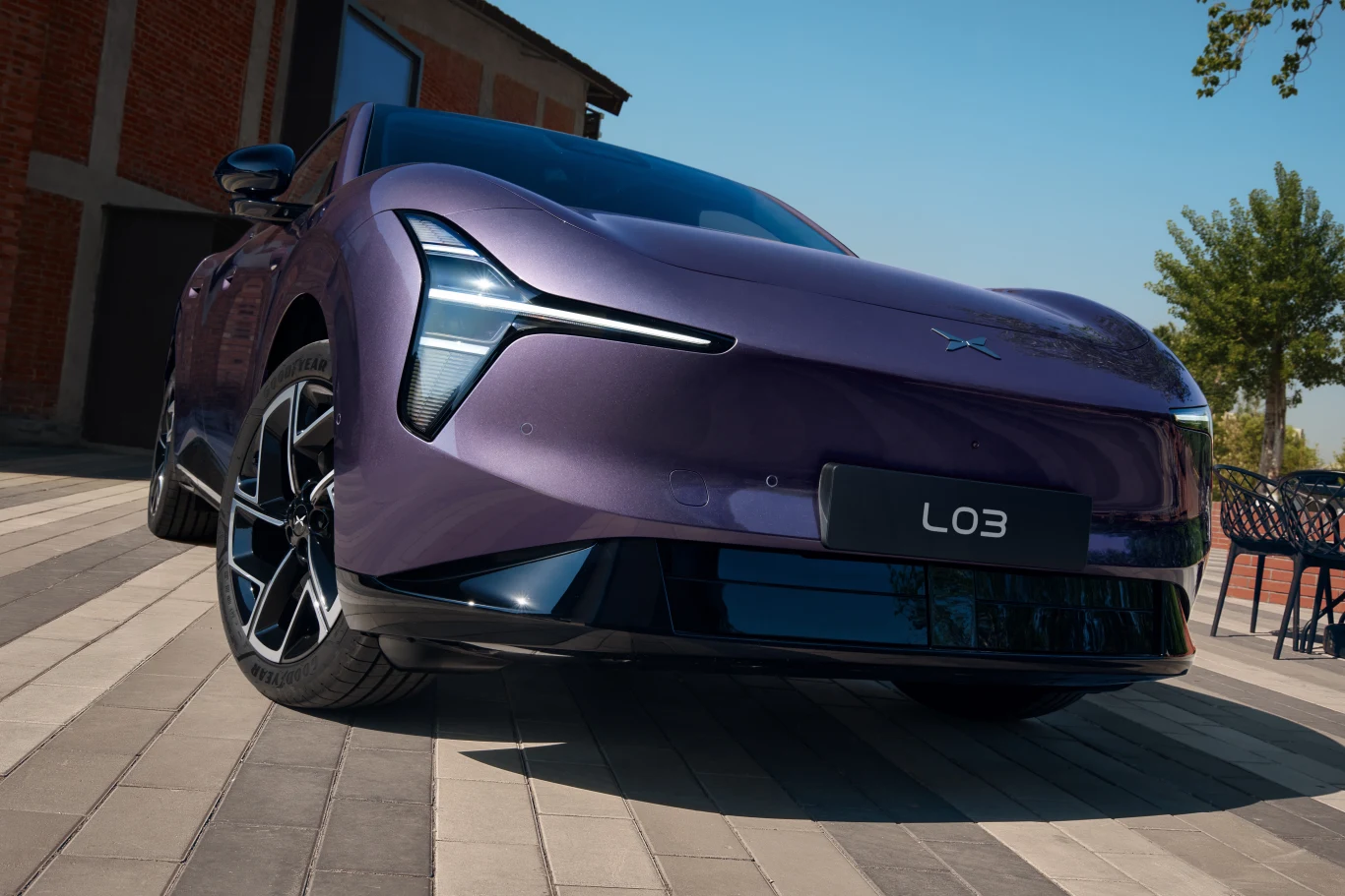 Fioletowy samochód elektryczny o futurystycznym designie i nowoczesnych reflektorach LED zaparkowany na brukowanym podjeździe obok budynku z cegły.
